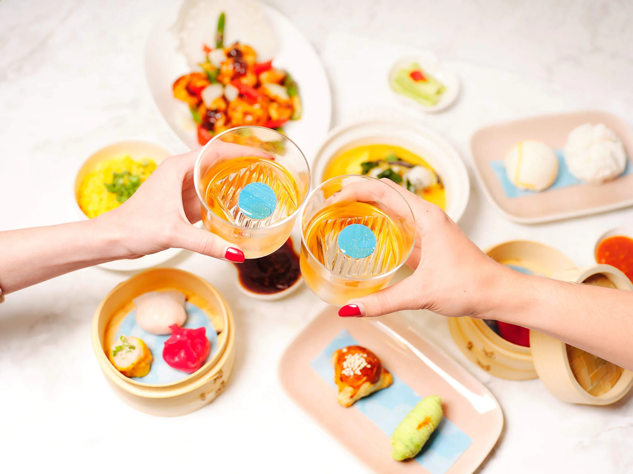 Hands clinking glasses over different plates of dim sum.